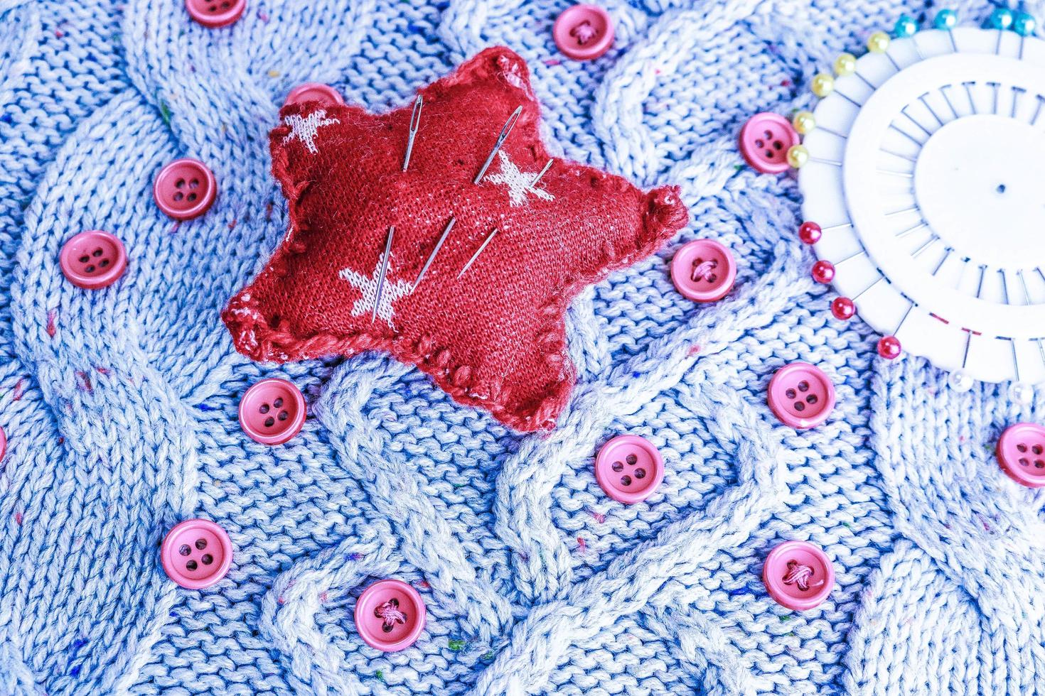 skön textur av en mjuk värma naturlig Tröja, stickat tyger och röd små runda knappar för sömnad och en nål vaddera. platt lägga. de bakgrund foto
