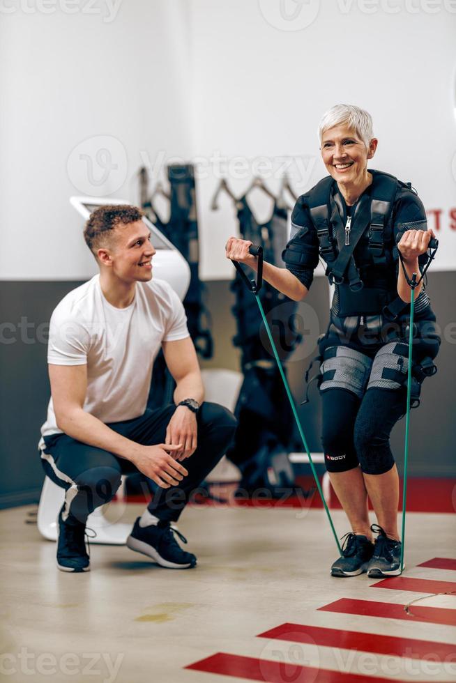 senior kvinna håller på med ems träna med tränare i de Gym foto