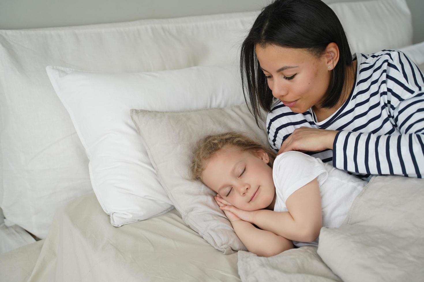 mamma tar antogs liten barn dotter till bekväm säng för sömn på mjuk kudde i Hem sovrum foto