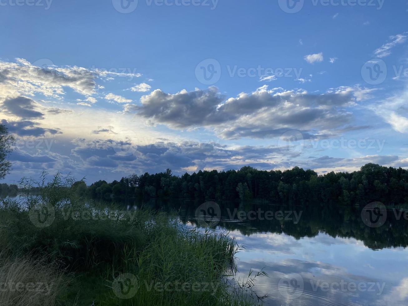 skön solnedgång på de sjö. moln och de silhuett av träd är reflekterad i de vatten. foto