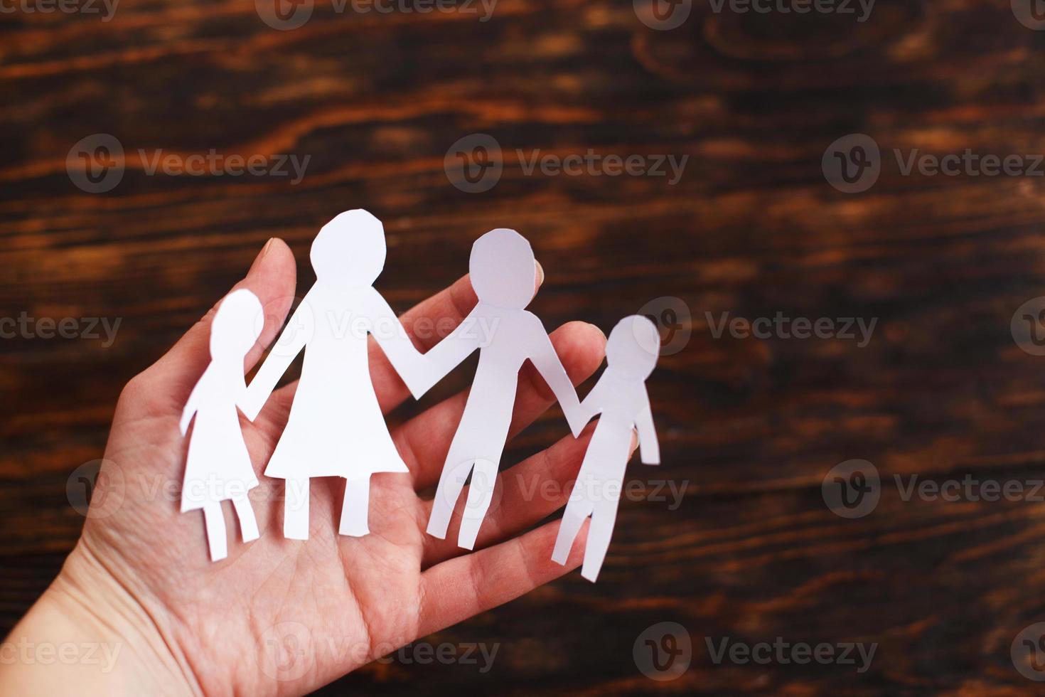 mänsklig hand innehav Lycklig papper skära familj på en brun trä- bakgrund foto