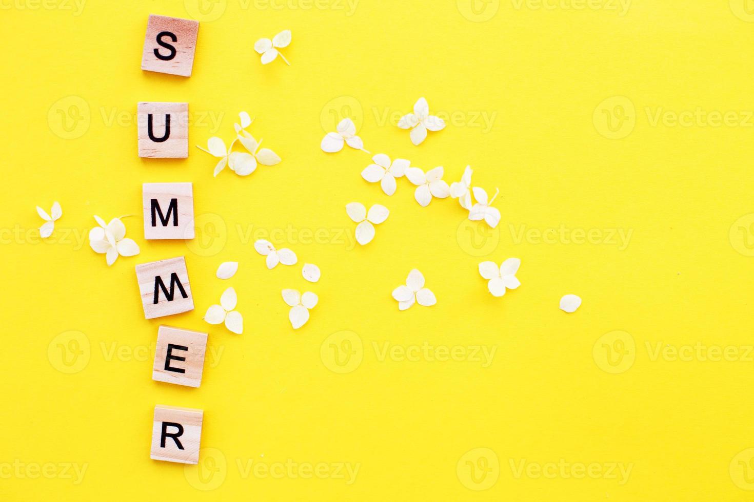 ord sommar skriven från en trä- kuber med brev på gul bakgrund med en kronblad av en hortensia blommor foto