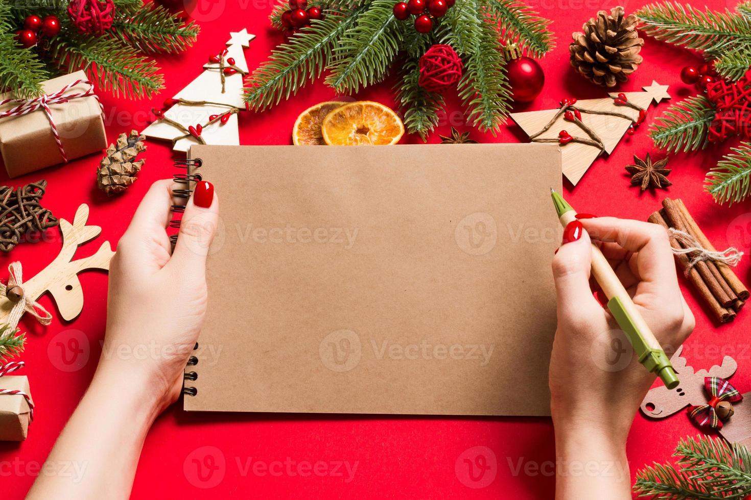 topp se av kvinna hand framställning några anteckningar i anteckningsbok på röd bakgrund. ny år dekorationer och leksaker. jul tid begrepp foto