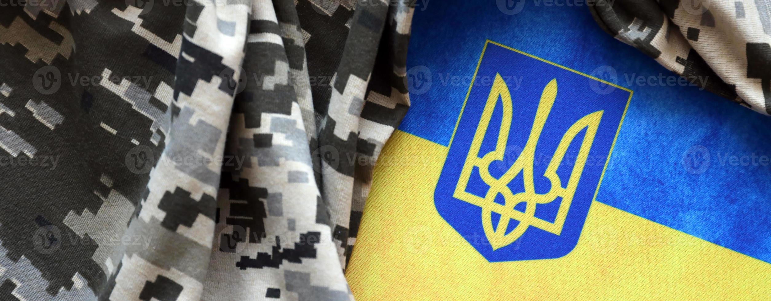 ukrainska flagga och täcka av vapen med tyg med textur av pixeled kamouflage. trasa med camo mönster i grå, brun och grön pixel former med ukrainska treudd tecken foto