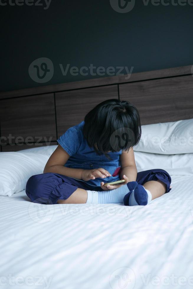 barn flicka tittar på tecknad serie på smart telefon på säng foto