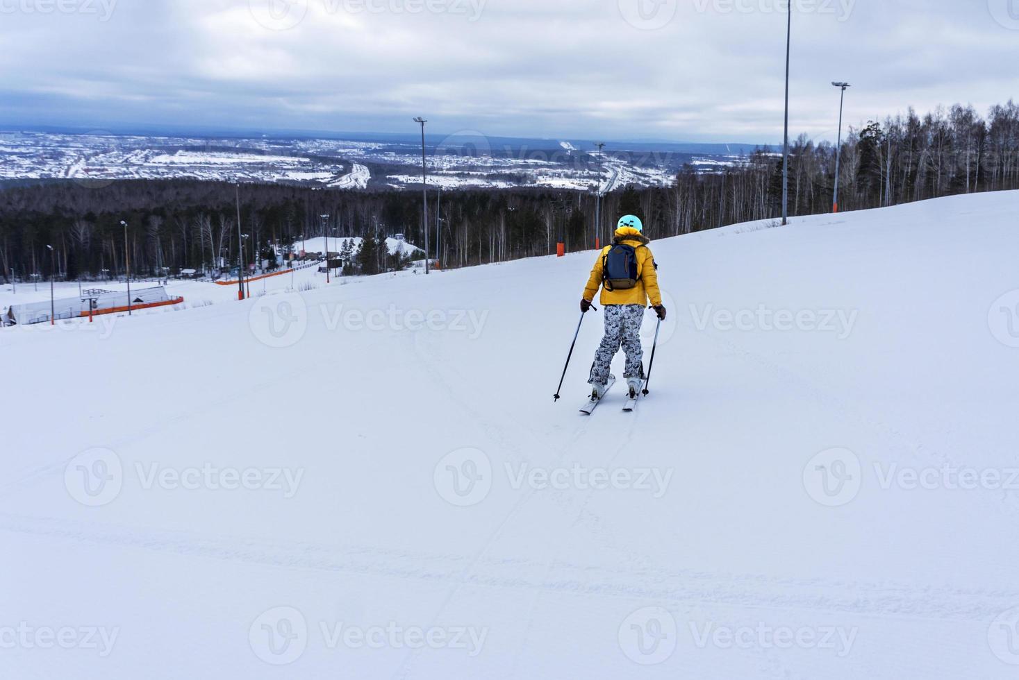 ung kvinna i gul jacka och åka skidor hjälm skidåkning ner på berg backe, vinter- sporter, alpina skidåkning utomhus aktivitet, friska livsstil foto