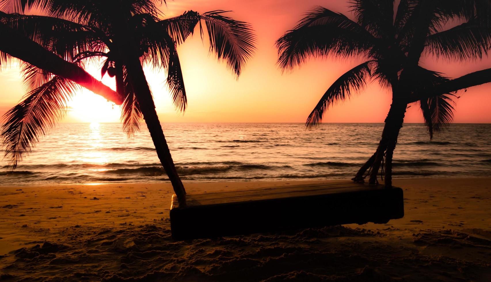 silhuett av handflatan träd och trä- gunga på de strand under solnedgång av skön en tropisk strand på rosa himmel bakgrund foto