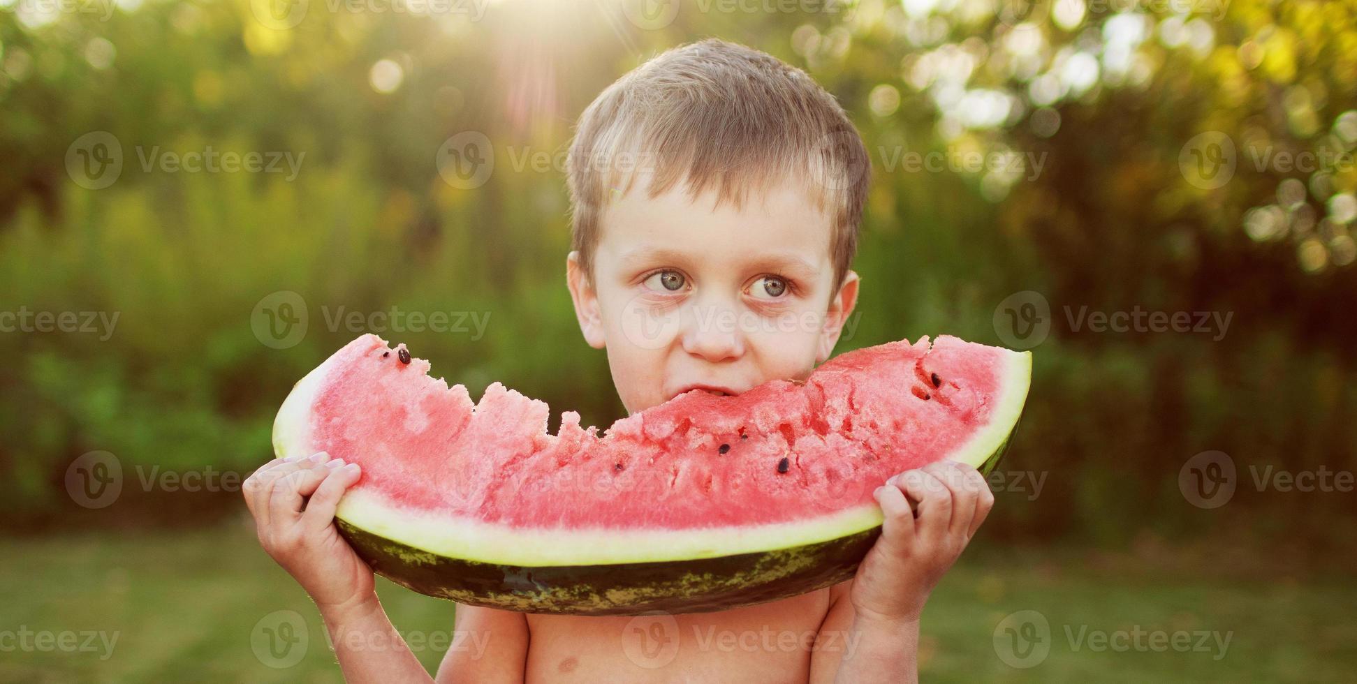 Lycklig leende barn pojke äter de vattenmelon utomhus- i de bakgård. baner foto