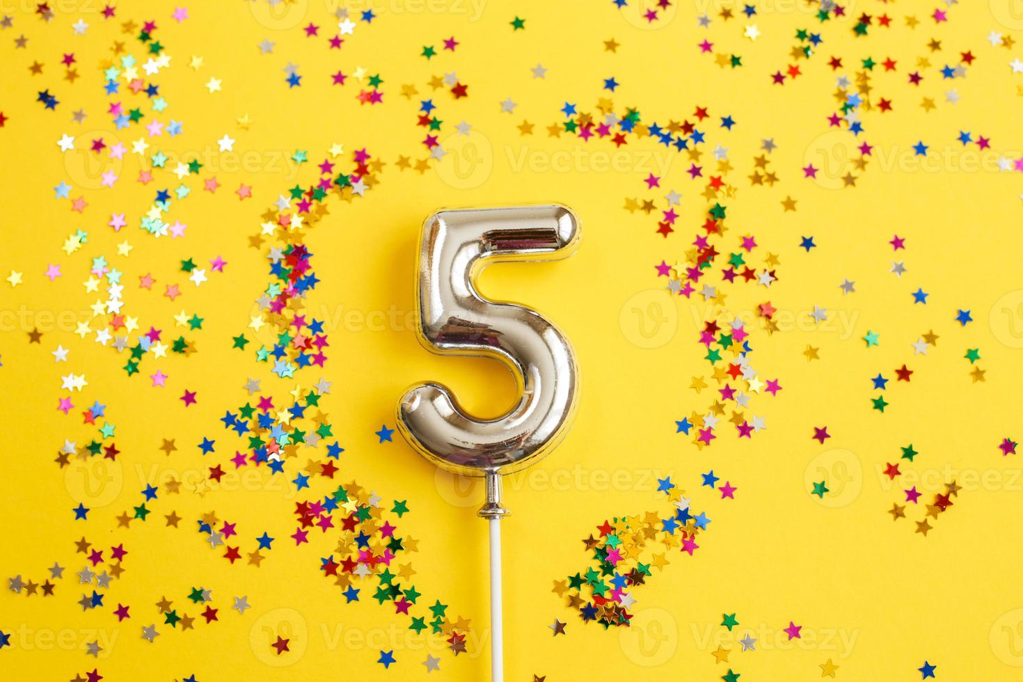 fem år födelsedag fest. siffra fem med flerfärgad konfetti i de form av stjärnor på en gul bakgrund foto