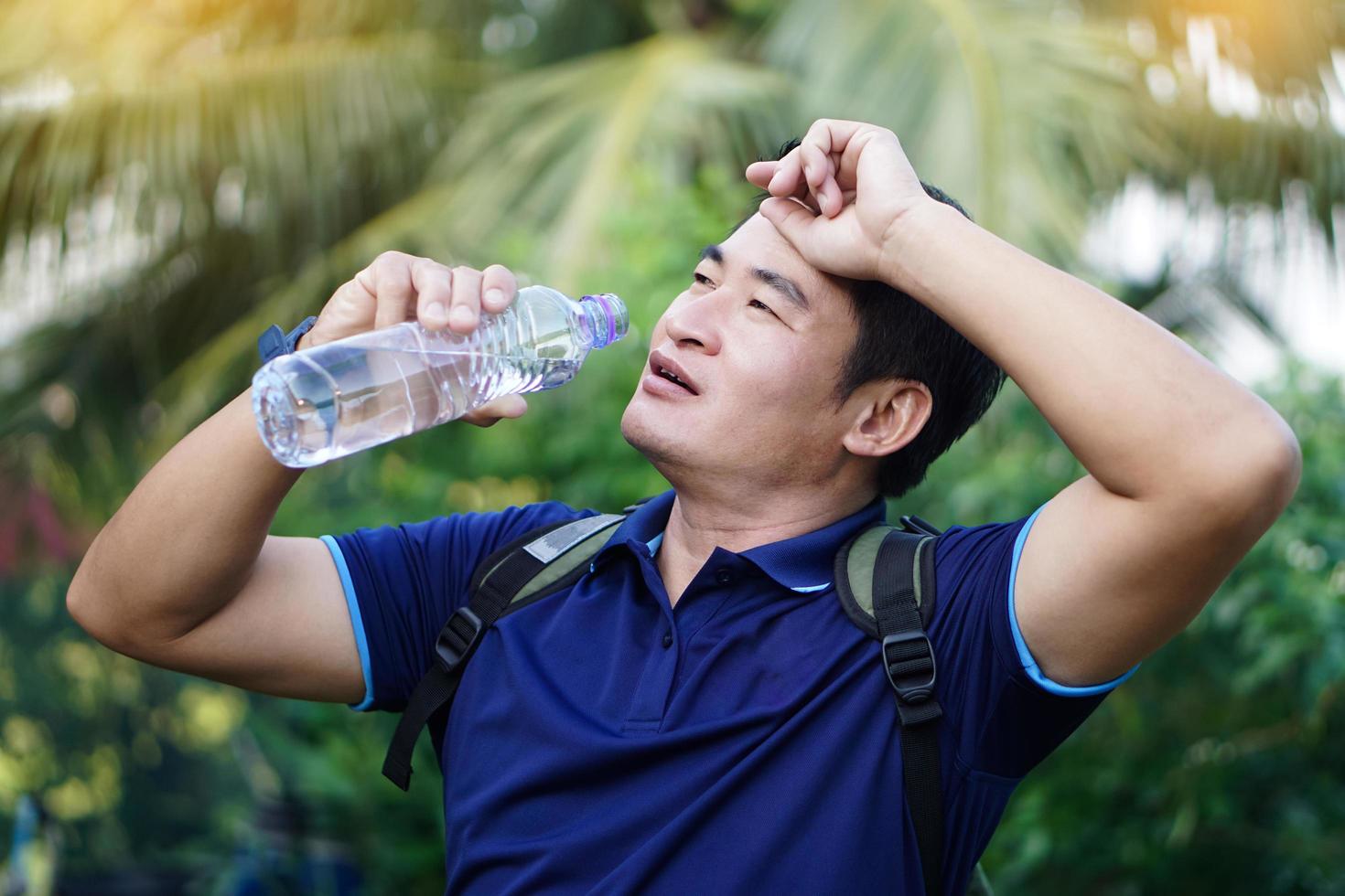 stilig asiatisk man resande innehar flaska av dricka vatten till dryck utomhus. begrepp , dricka vatten för hälsa, friska livsstil.släckning törst, minska Trötthet, uppdateras kropp. foto