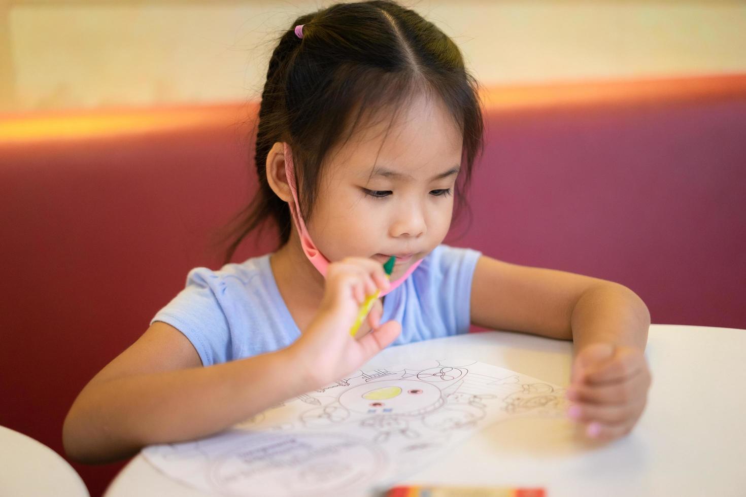 liten flicka sitter vid bordet och ritar bilder med pennor foto