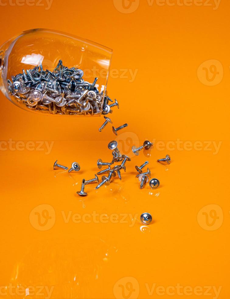 tappade många metall självuttag skruvar tillverkad av stål i en glas, i hink burk. självuttag skruva för metall, för järn, förkromad självuttag skruva, på ett orange gul bakgrund, foto