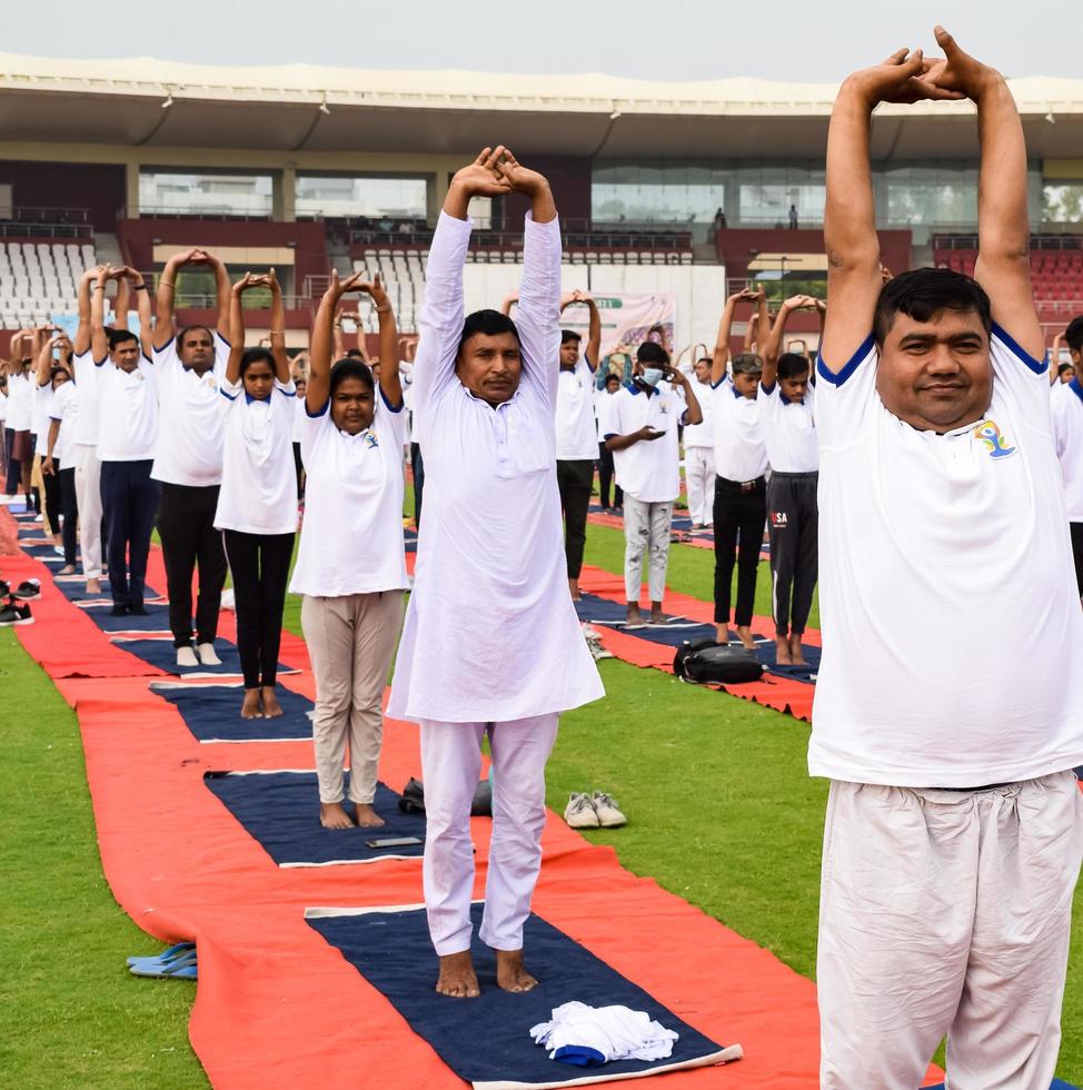 ny delhi, Indien, juni 21 2022 - grupp yoga övning session för människor på yamuna sporter komplex i delhi på internationell yoga dag, stor grupp av vuxna delta yoga klass i cricket stadion foto