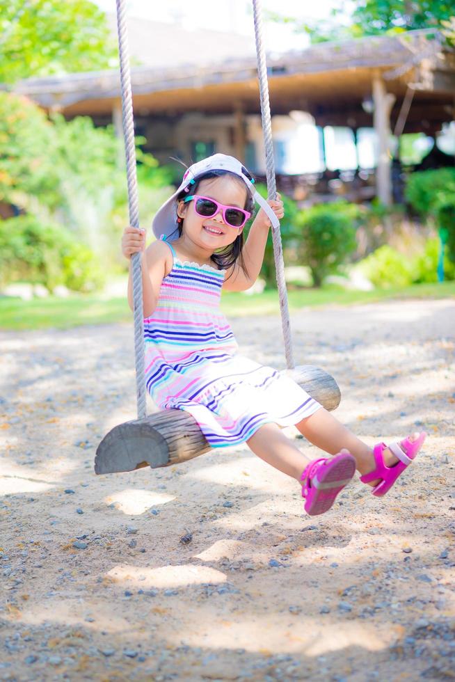 liten flicka bär solglasögon på en gunga i parken foto