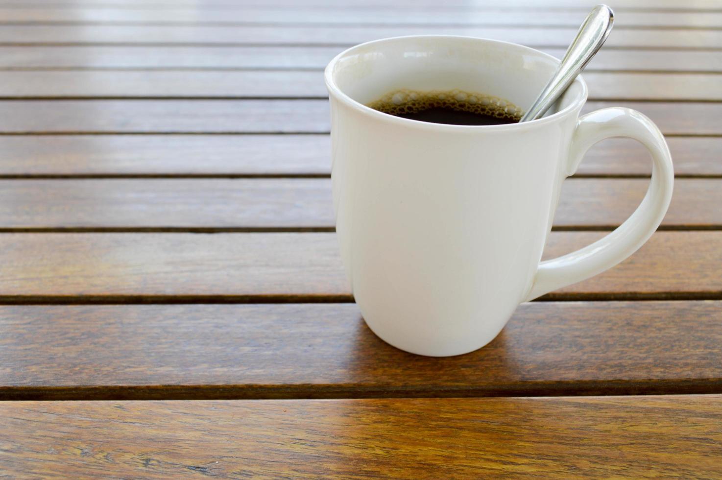 en vit keramisk kopp med en morgon- uppfriskande varm kaffe med te dryck och te skinande tesked är på en trä- tabell i en Kafé foto