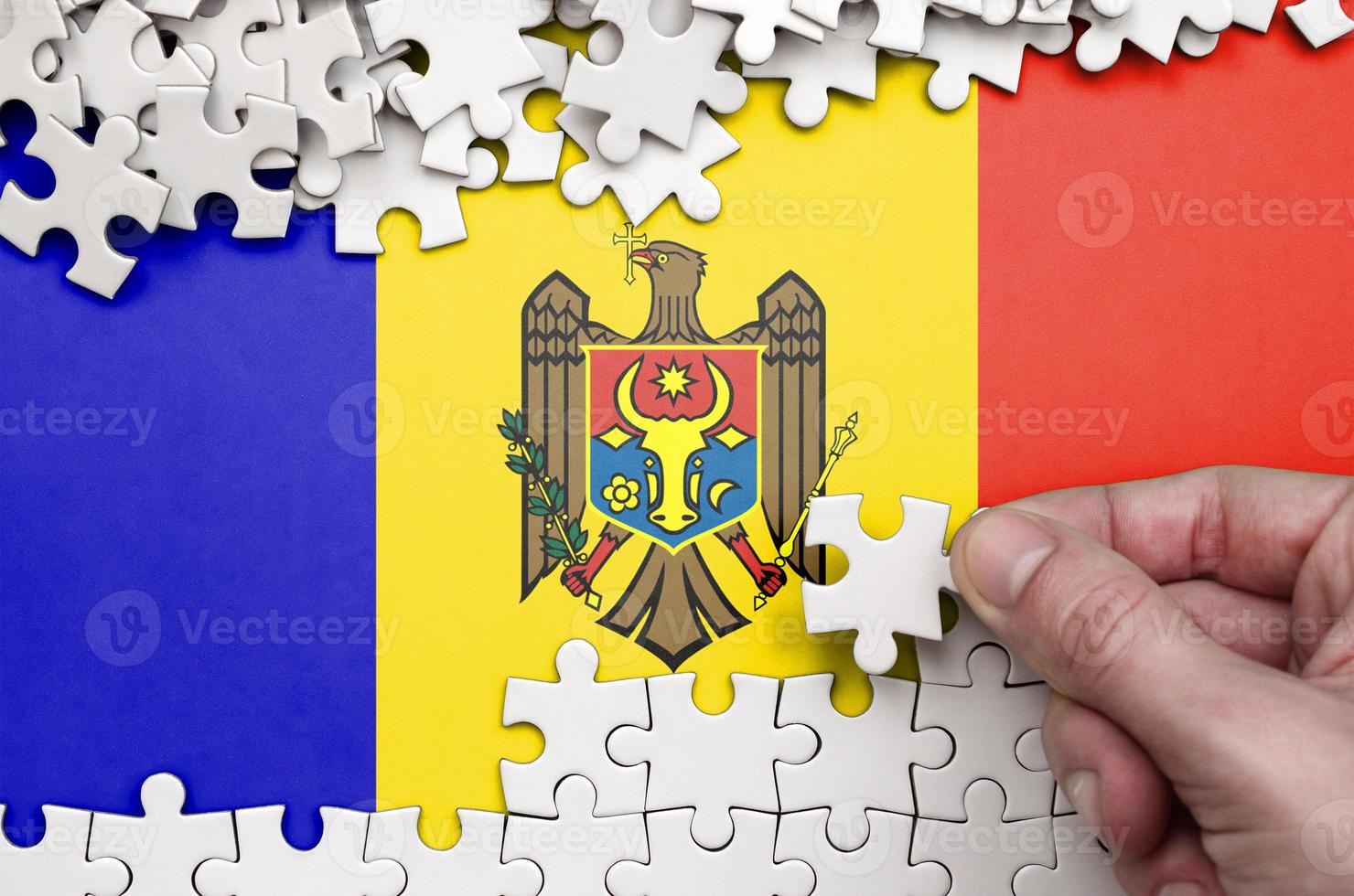 moldavien flagga är avbildad på en tabell på som de mänsklig hand veck en pussel av vit Färg foto