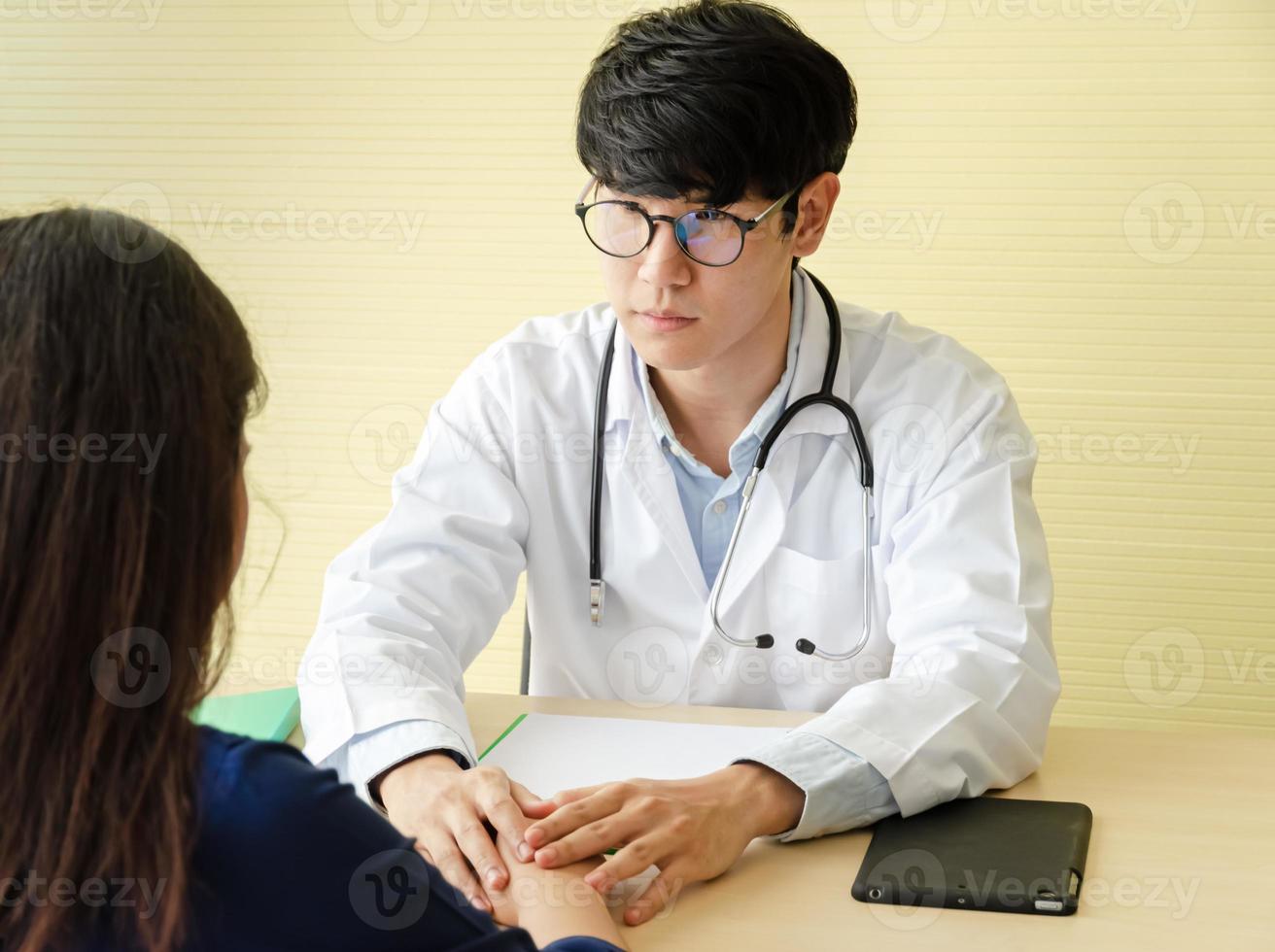 ung asiatisk läkare händer innehav kvinna patient hand för uppmuntran och empati i kontor foto