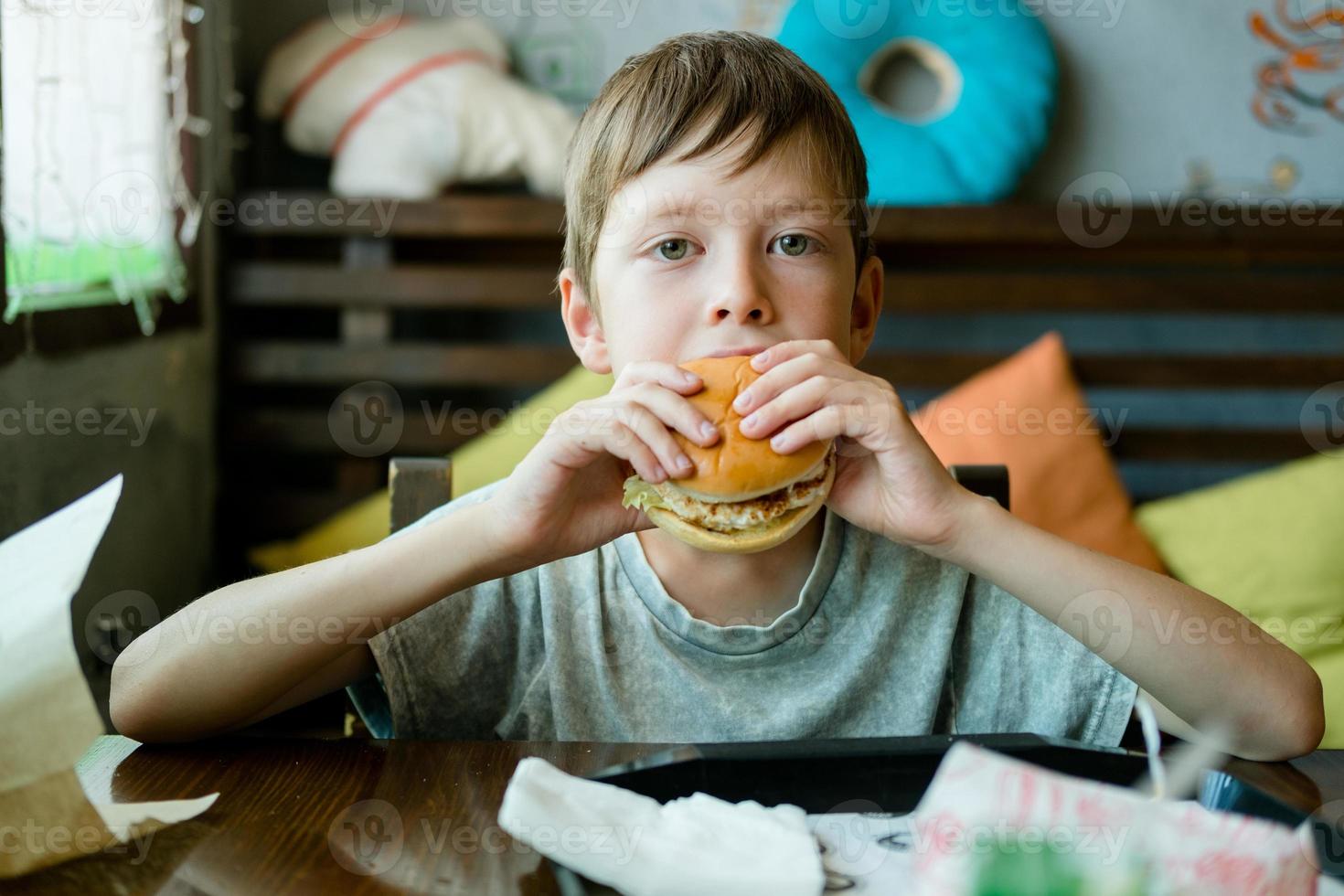 pojke äter en stor burger med en kotlett. hamburgare i de händer av en barn. utsökt och tillfredsställande kyckling kotlett hamburgare. ta ut mat foto