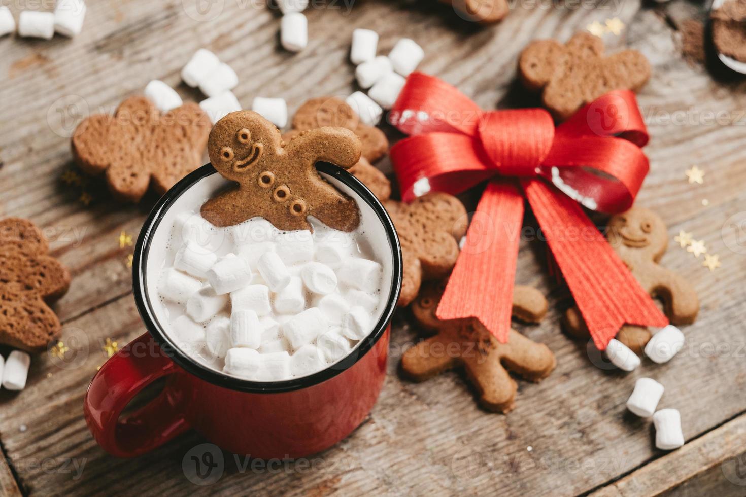 ingefära man i en kopp av kakao med en stor röd rosett på en trä- bakgrund, topp se. olika jul sötsaker med en kopp av kakao på de tabell. jul flatlay foto