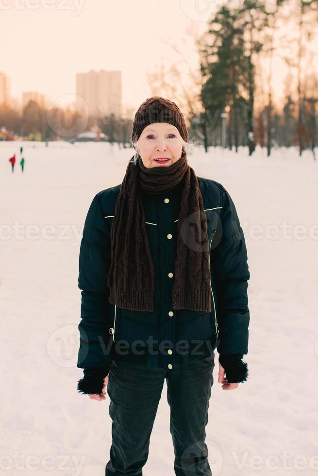 senior kvinna i hatt och sportig jacka joggning och håller på med sporter övningar i snö vinter- parkera. vinter, ålder, sport, aktivitet, säsong begrepp foto