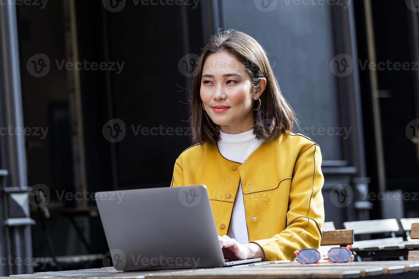 ung skön asiatisk kvinna Sammanträde i kaffe affär på trä- tabell, dricka kaffe och använder sig av bärbar dator. flicka bläddring internet, chattar, bloggar. kvinna använder sig av bärbar dator och ser på hans skärm. foto