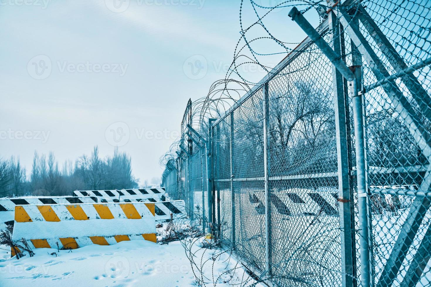 hullingförsedda tråd staket på gräns med betong väg block på jord i vinter. foto