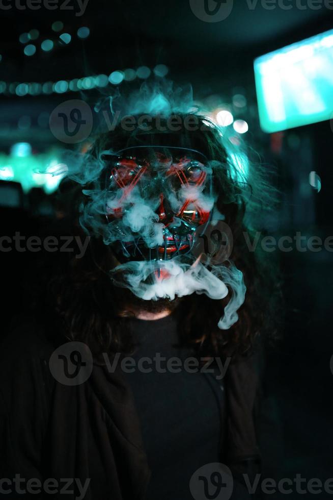 man i huva med lång rufsig hår i en belysning neon lysande mask. foto