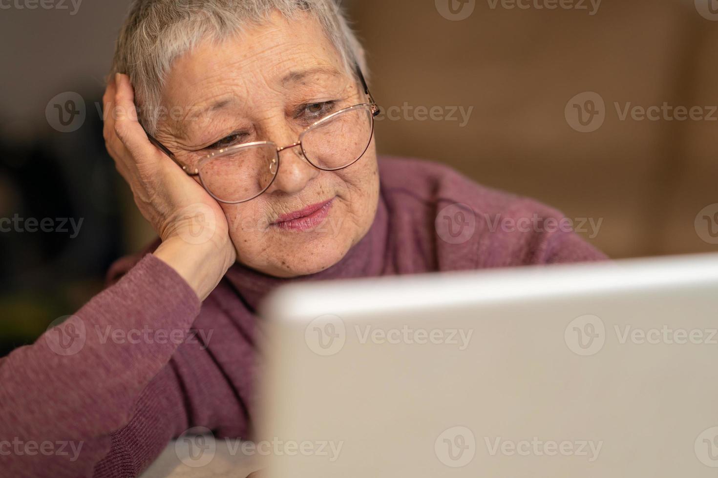 en senior kvinna Sammanträde i främre av en bärbar dator kommunicerar uppkopplad genom social nätverk. foto