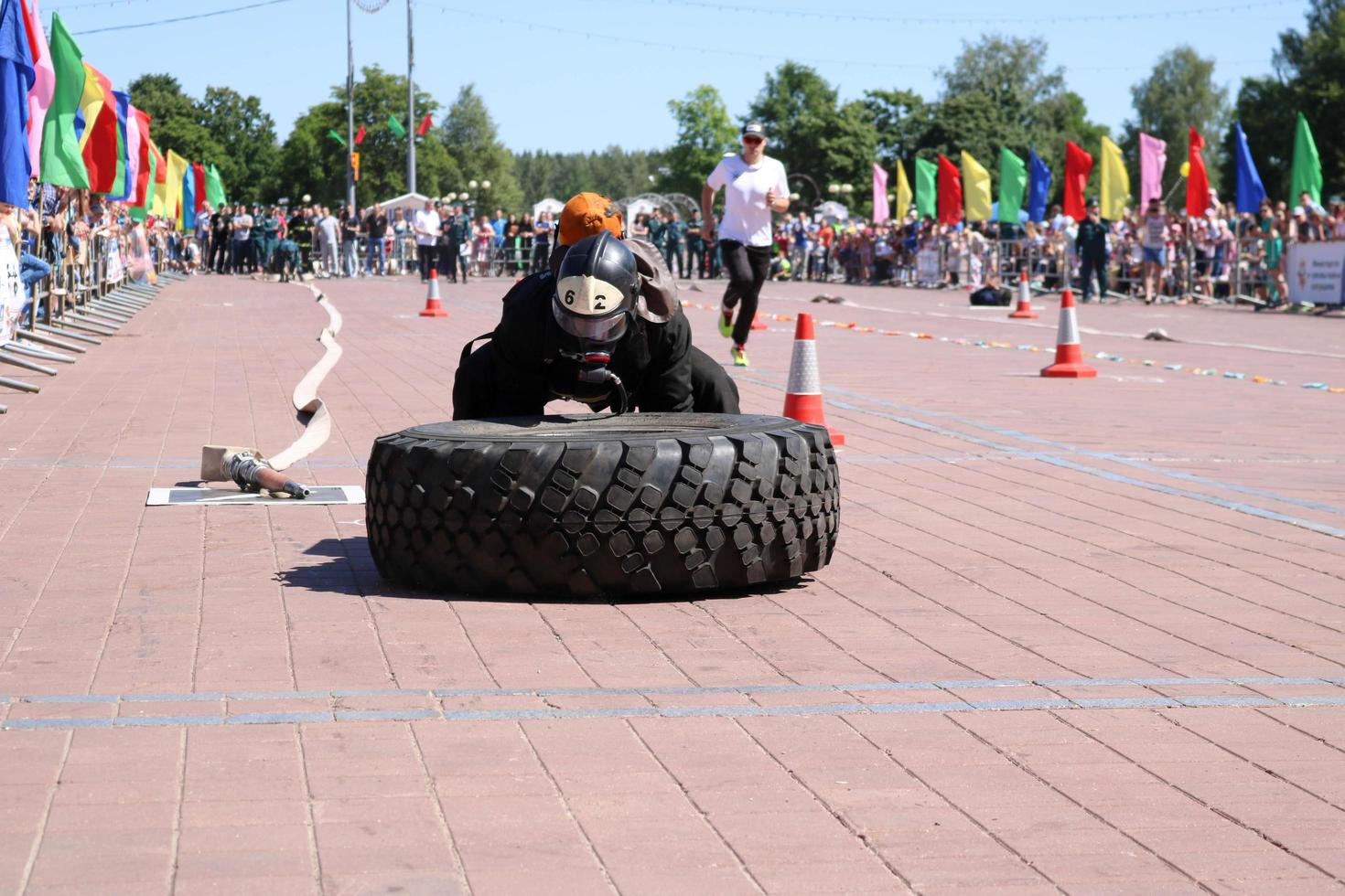 en brandman i en eldfast kostym och en hjälm kör och vänder en stor sudd hjul i en brand stridande konkurrens, belarus, minsk, 08.08.2018 foto