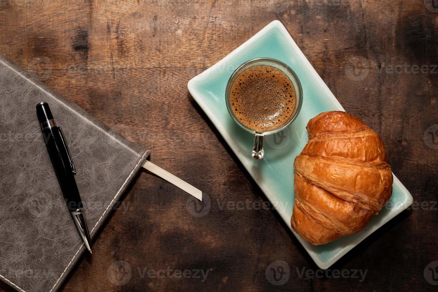 frukostmat croissant i tallrik och kaffe på träbord. foto