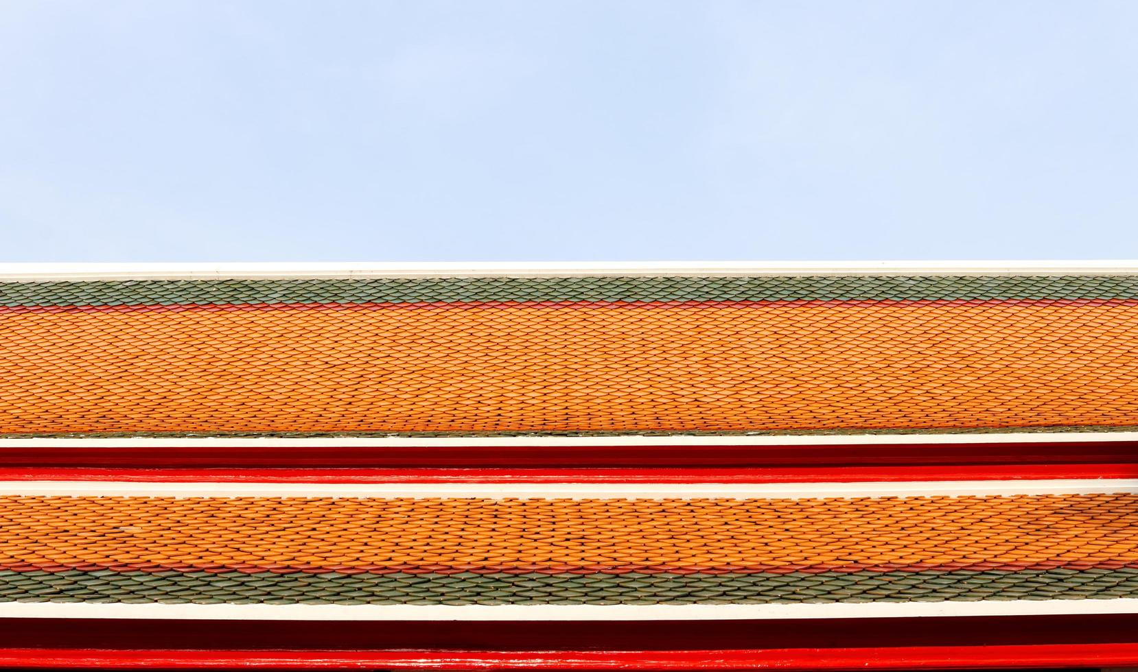 gammal stil av keramisk bricka tak mönster och ljus blå himmel. grön, röd, orange Färg rad av plattor på taket i tempel, thailand. foto