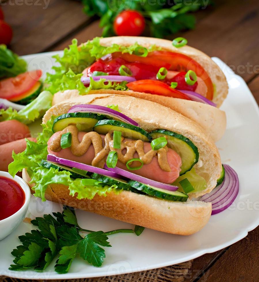 hotdog med ketchup, senap, sallad och grönsaker på träbord foto