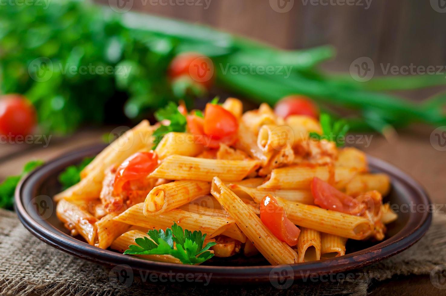 penne pasta i tomat sås med kyckling och tomater på en trä- tabell foto