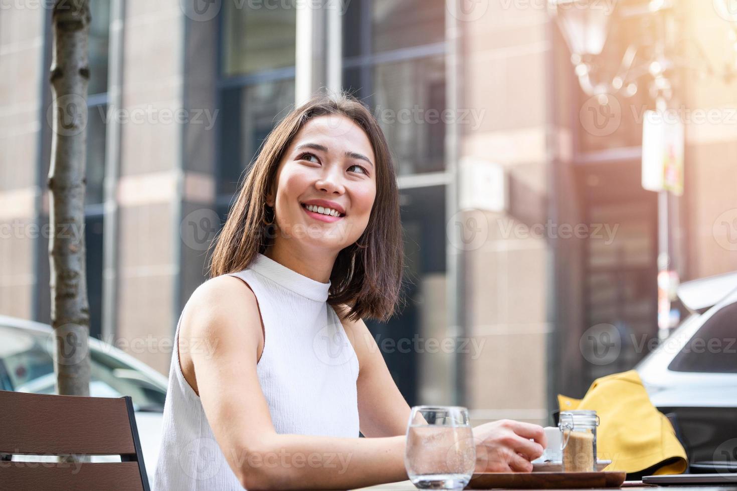 skön asiatisk ung kvinna med kopp av kaffe. kvinna åtnjuter färsk kaffe i de morgon- med soluppgång på coffe affär skön kvinna dricka kaffe i de morgon- Sammanträde utomhus foto