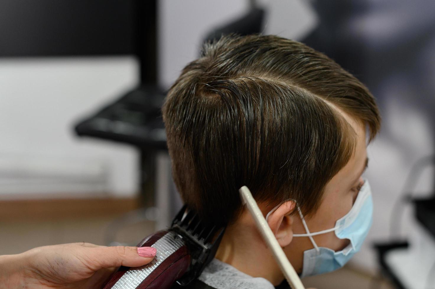 en tonåring i en skönhetssalong klipper sig, en frisör klipper en tonårspojkes hår. foto