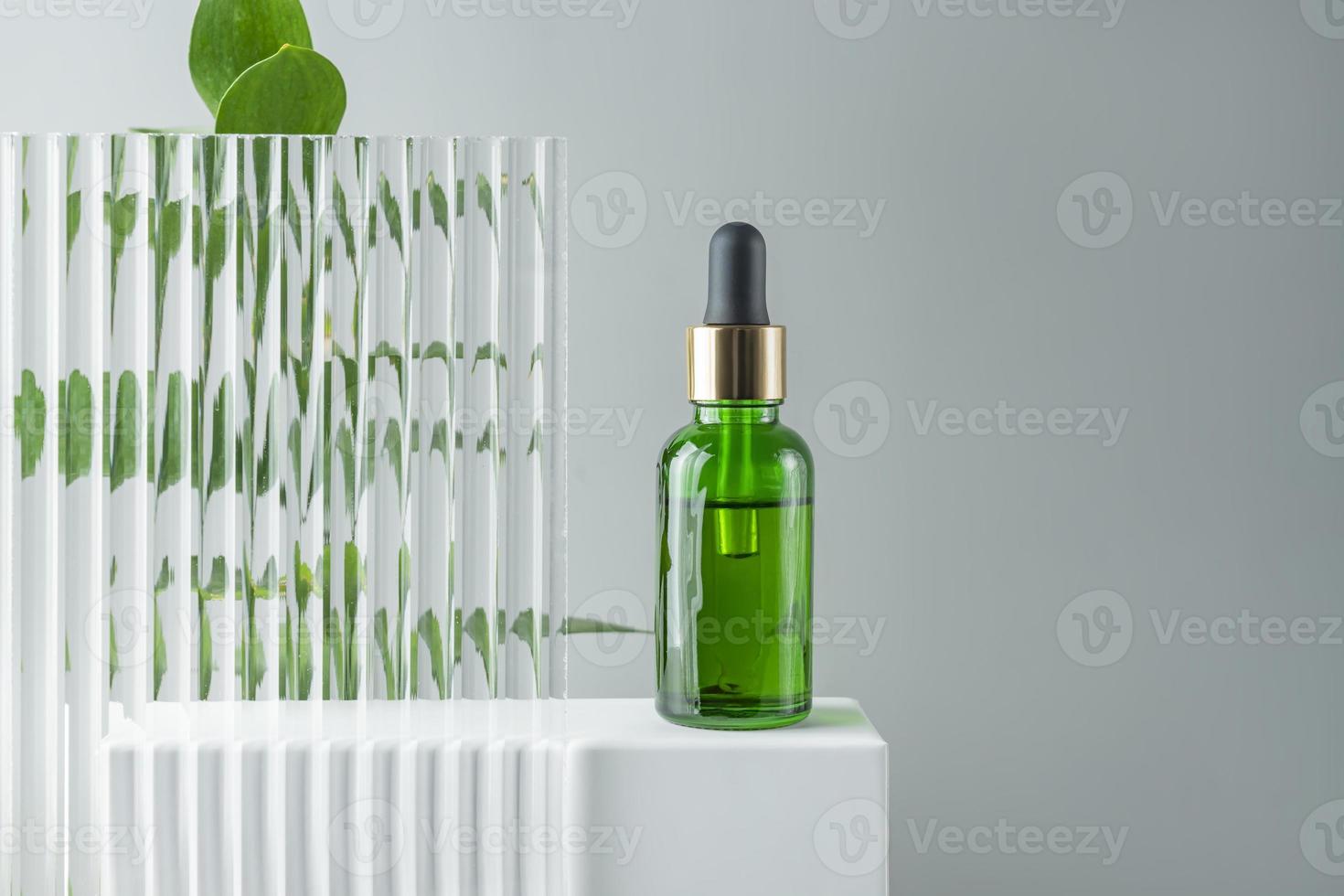 kosmetisk flaska serum, olja på vit stå med grön gren på grå bakgrund. naturlig kosmetika begrepp, hud vård produkt. skönhet begrepp för ansikte kropp vård. attrapp foto