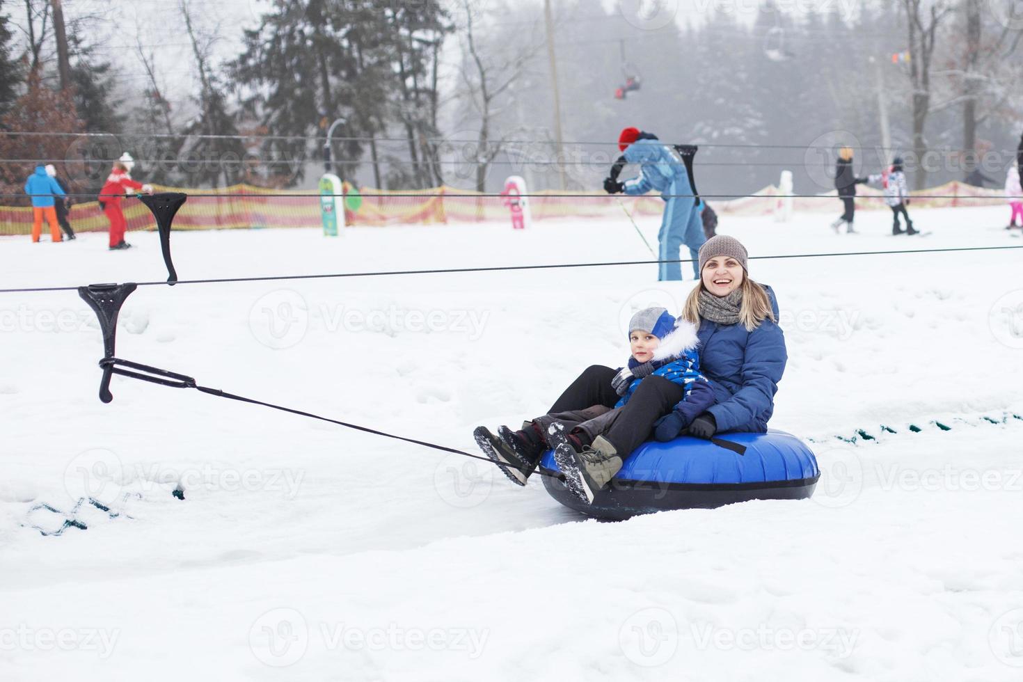 familj har roligt på snö rör. mor med unge är ridning en slang. människor glidning utför på rör. rida en hiss foto