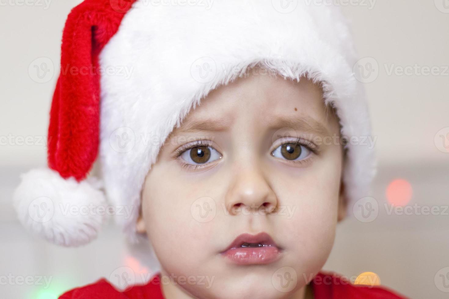 porträtt av en söt pojke i en santa claus hatt. rolig leende barn. gåvor, leksaker, glädje, firande. foto