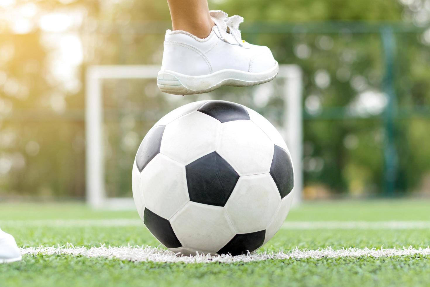 fötter av en pojke som bär vita sneakers som kliver på en fotboll foto