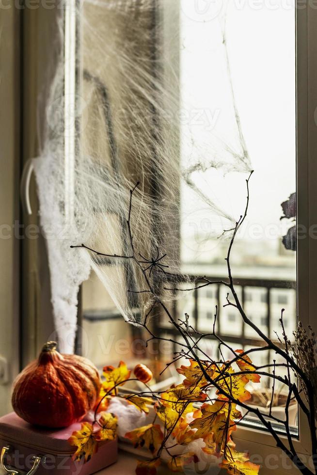 halloween begrepp, dekorerad fönster med spindelnät, höst gul löv, bar träd grenar och en pumpa på en mörk bakgrund foto