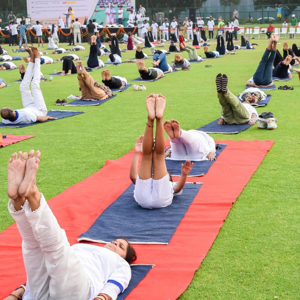 ny delhi, Indien, juni 21 2022 - grupp yoga övning session för människor på yamuna sporter komplex i delhi på internationell yoga dag, stor grupp av vuxna delta yoga klass i cricket stadion foto