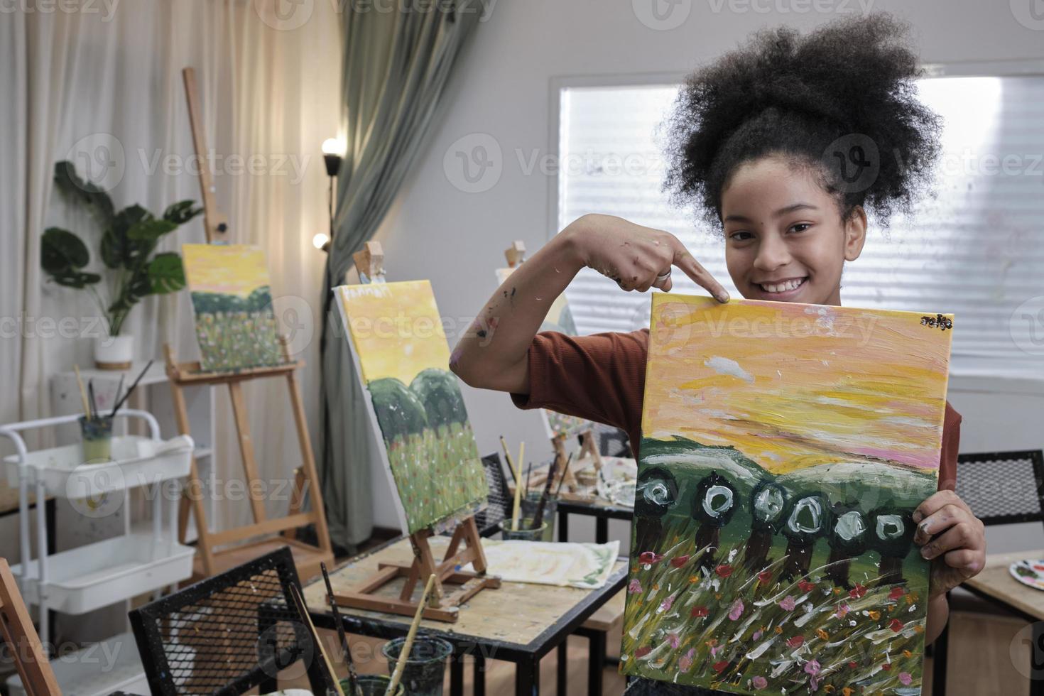 ett svart studerande flicka visar henne målning arbete, stolt med portfölj, akryl Färg bild på duk i konst klassrum och kreativ inlärning med talanger skicklighet på elementärt skola studio utbildning. foto