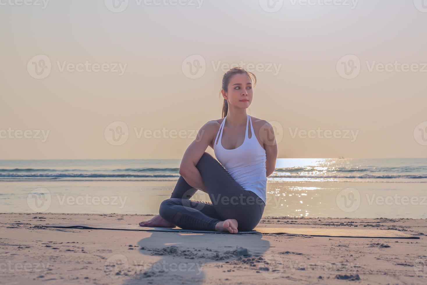 ung asiatisk friska kvinna håller på med yoga övning på de strand i de morgon. foto