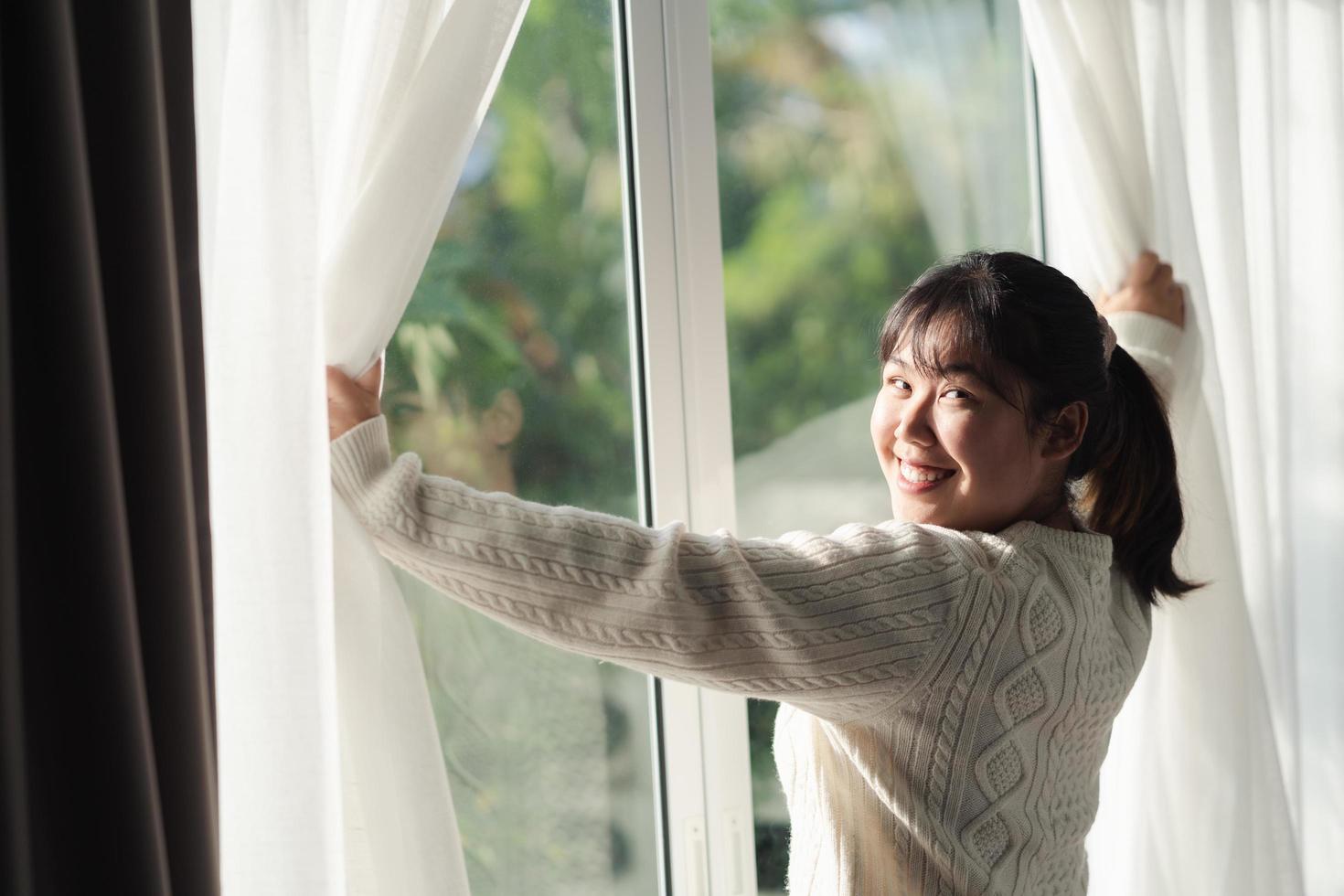 Lycklig kvinna öppning fönster gardiner i de morgon. foto