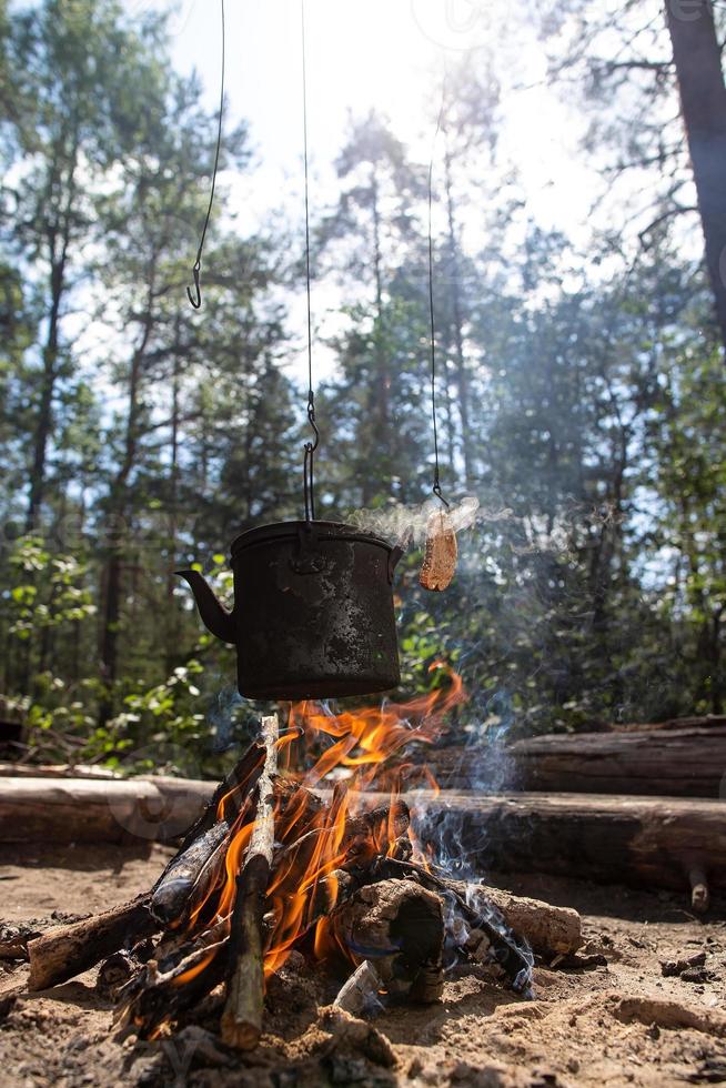 kokande vattenkokare med varm dryck och en skiva av friterad bröd över de lägereld i en skog, på en solig dag. frukost i de kampanj. foto