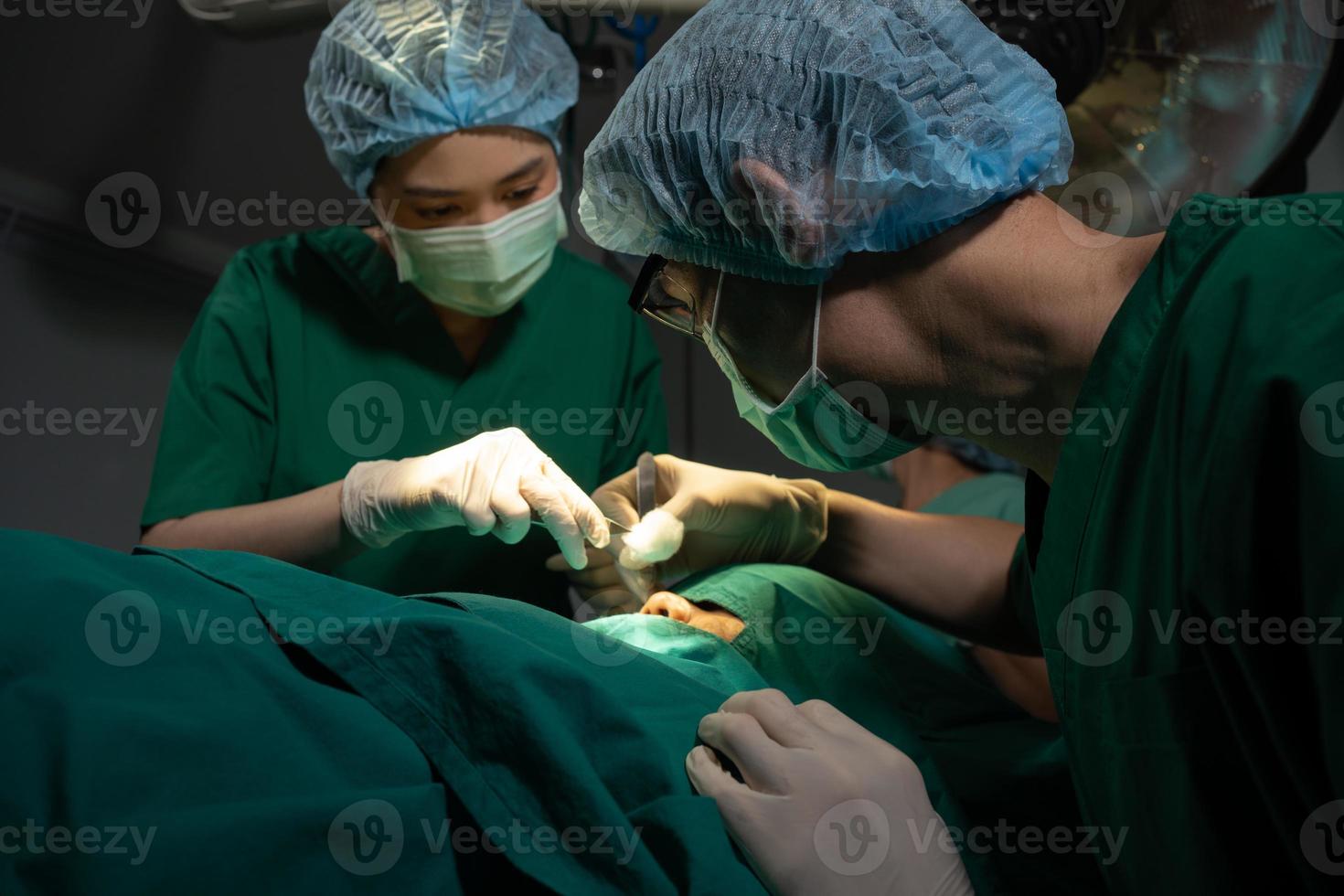 asiatisk professionell kirurger team utför kirurgi i de rörelse rum, kirurg, assistenter, och sjuksköterskor utför kirurgi på en patient, hälsa vård cancer och sjukdom behandling begrepp foto