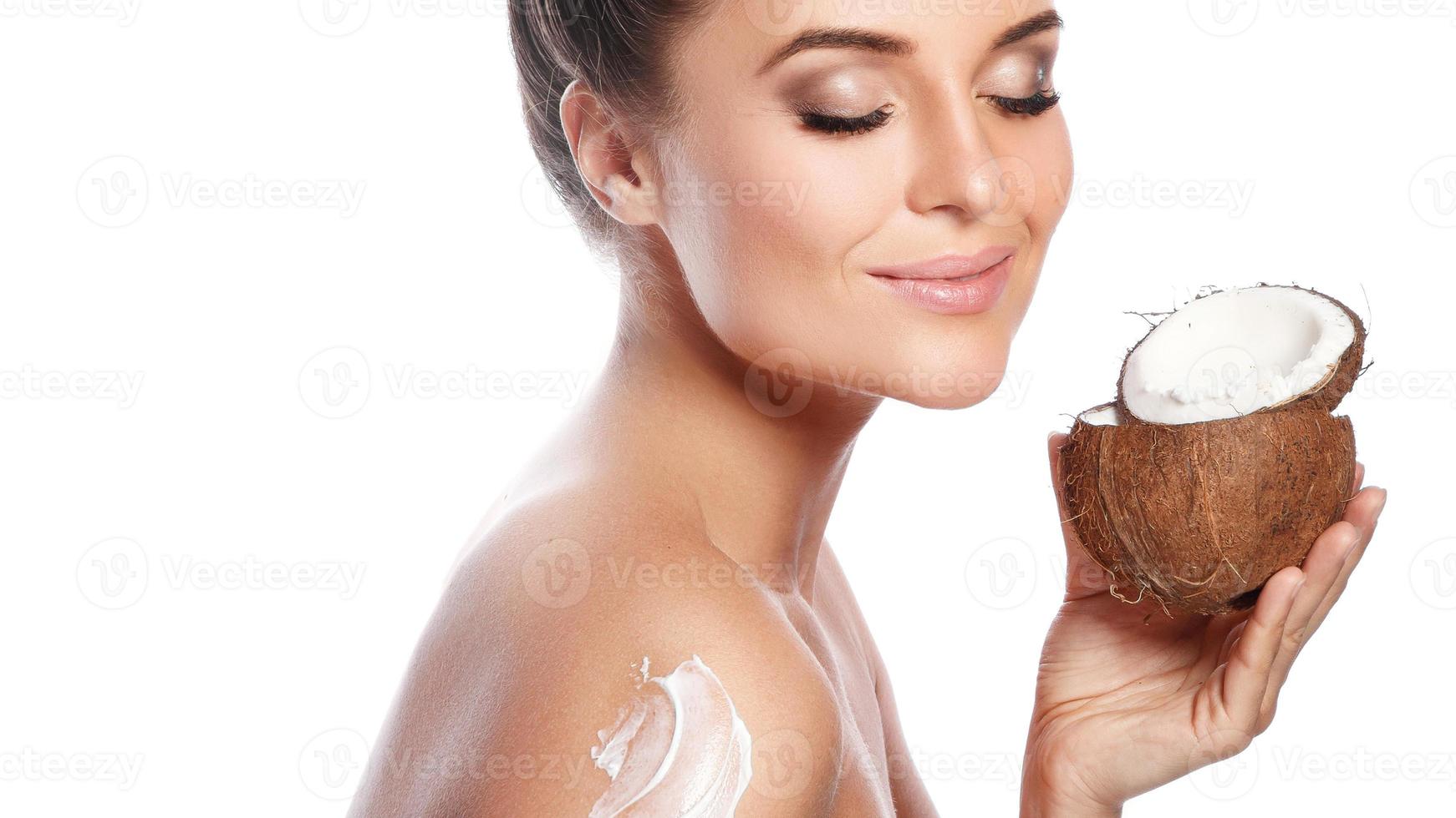 skön kvinna applicering grädde på henne kropp baserad på kokos olja på vit bakgrund foto