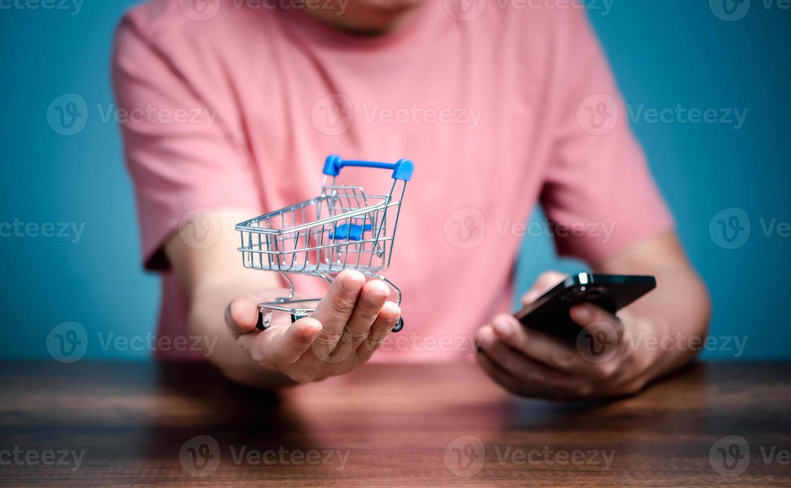 handla uppkopplad med handla vagn, man använder sig av mobil telefon köpa saker på webb sida affär. foto