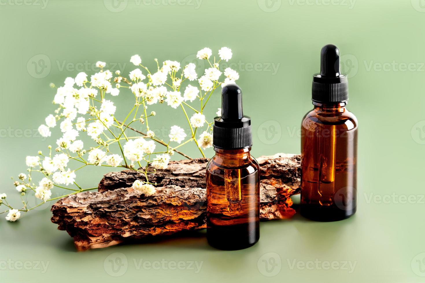 två flaskor med en dropper med en serum för hud vård av de ansikte mot de bakgrund av de bark av de träd och blommor. foto