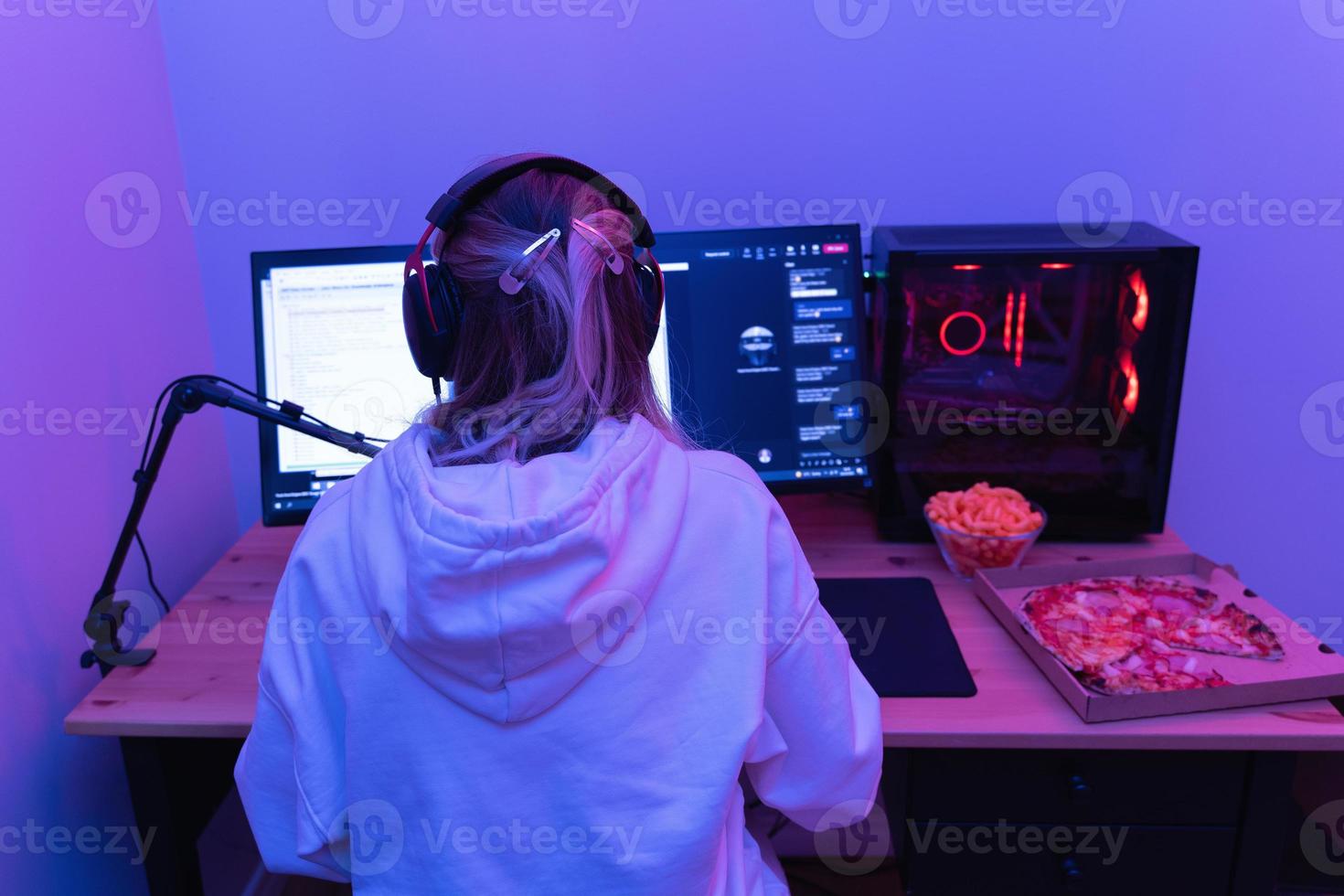 kvinna gamer eller programvara utvecklare Sammanträde på de modern personlig dator och äter skräp mat på natt i rum med neon lampor foto